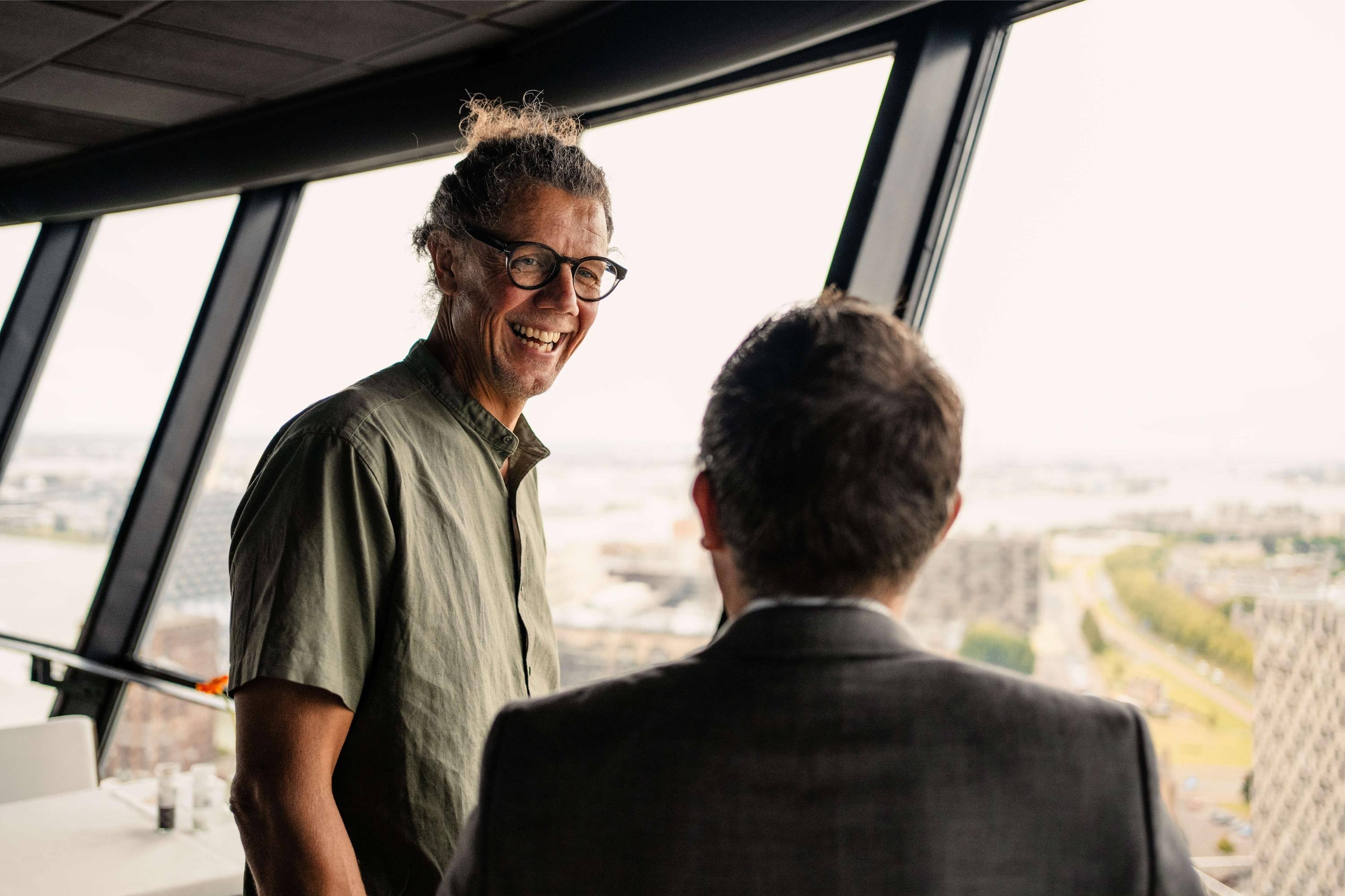 Christian Schulze Dieckhoff unterhält sich lächelnd mit einem anderen Mann vor einer Fensterfront.