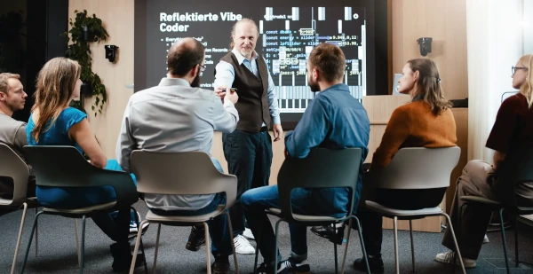 Bild von einem Event bei der viadee Unternehmensberatung. Ein Referent steht vor einem Monitor auf dem Folien zum Thema Vibe-Coding in der IT zu sehen sind. Im Vordergrund sieht man von hinten Teilnehmende IT-Führungskräfte und IT-Entscheider:innen, die dem Event folgen.