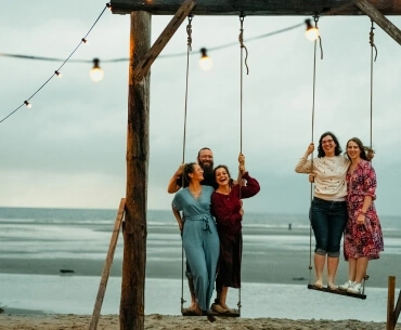 Mitarbeiter:innen der viadee stehen auf zwei Schaukeln am Strand und lachen.