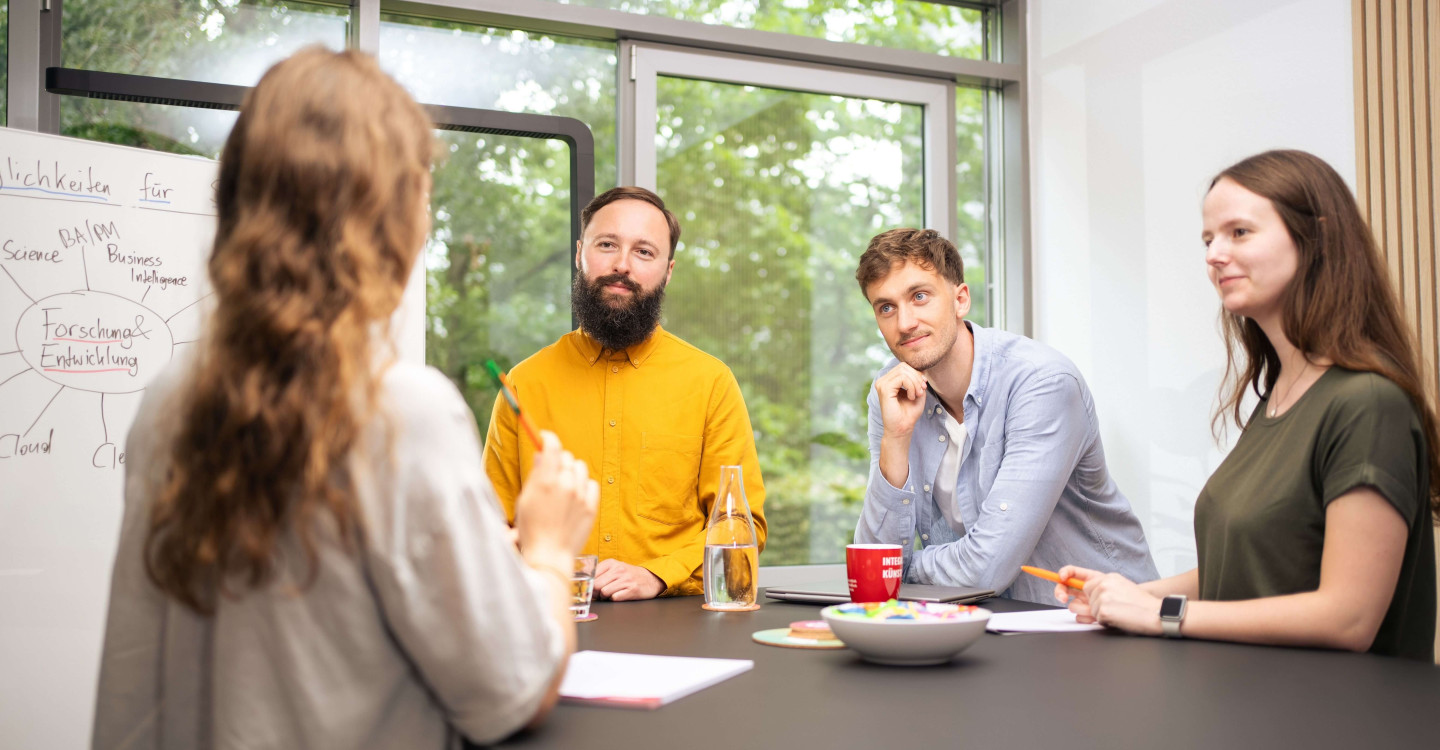 Drei Werkstudierende der viadee stehen mit einem Hochschulkoordinator der viadee um einen Arbeitstisch und arbeiten zusammen.