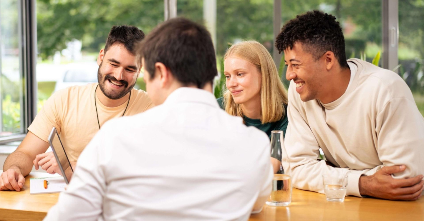 Vier Werkstudierende der viadee sitzen an einem Tisch und betrachtet etwas auf einem Laptop.
