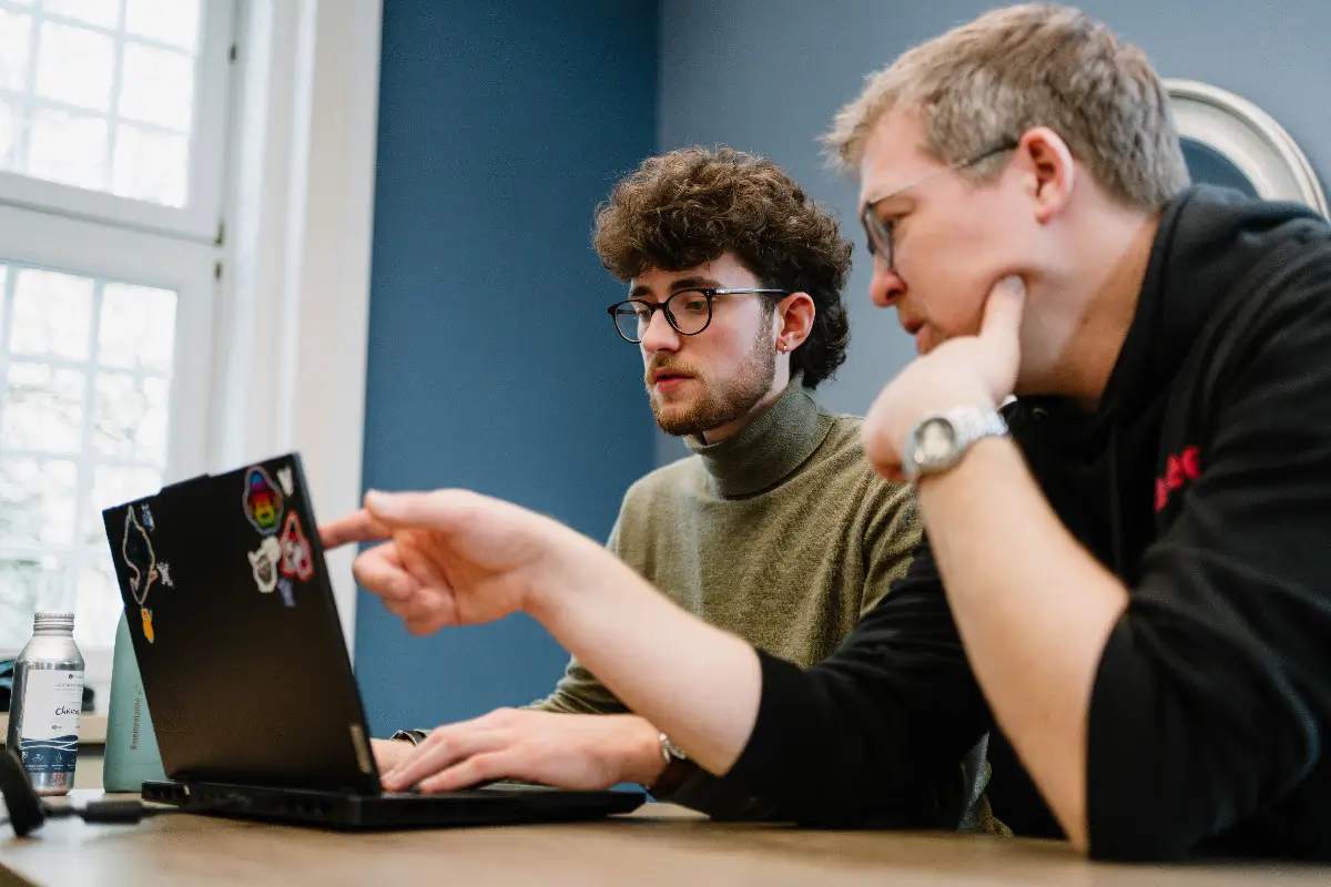 Zwei Berater der viadee sitzen an einem Tisch und arbeiten zusammen mit einem Laptop.