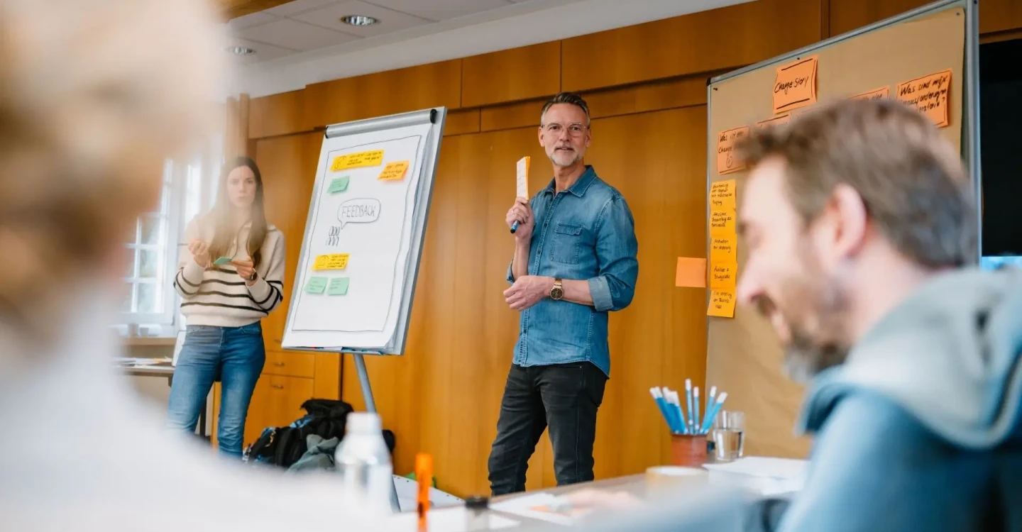 Vier Berater:innen der viadee sitzen in einem Workshop. Zwei präsentieren und leiten den Workshop an einem Flipboard.