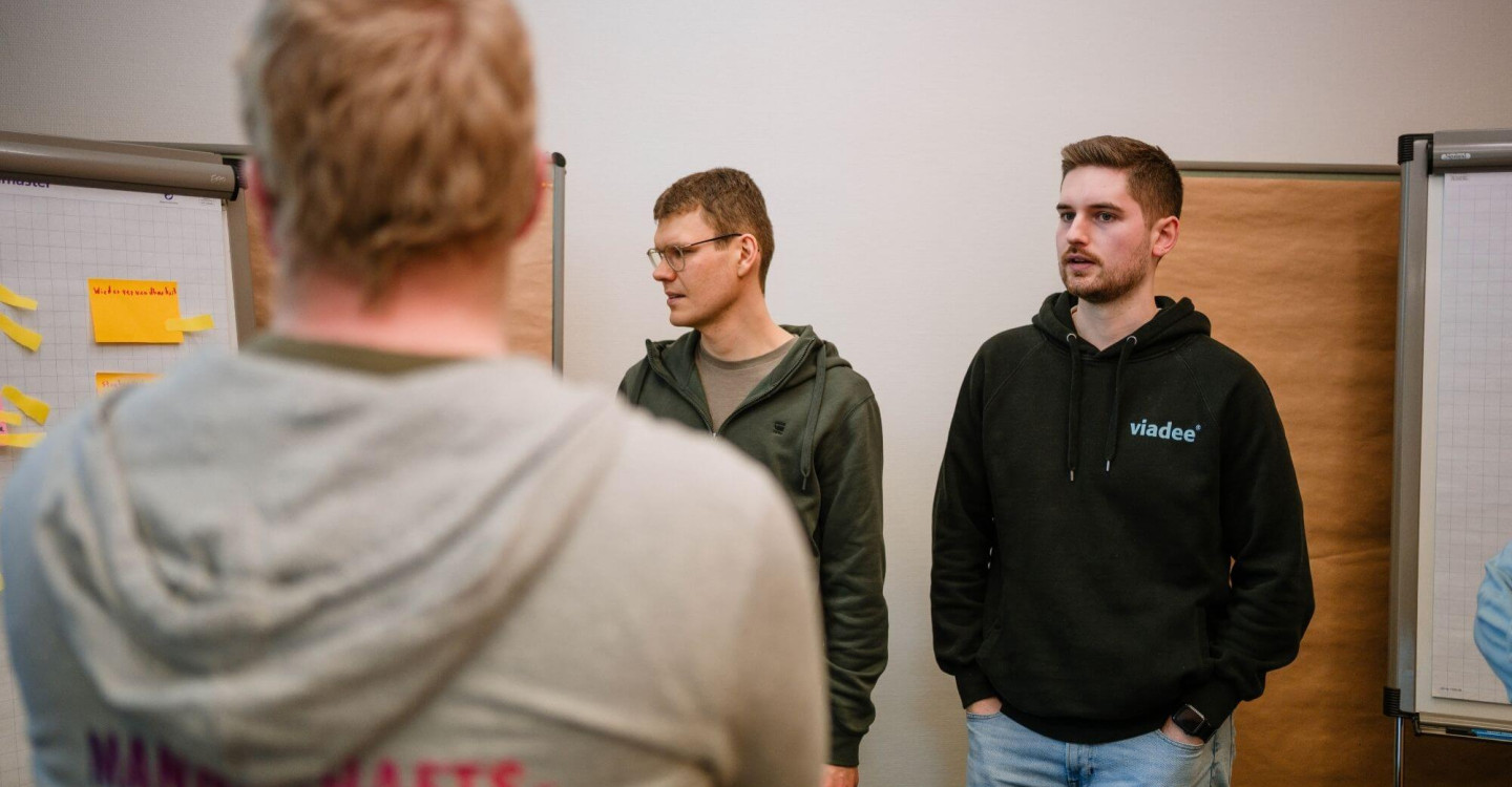 Drei Mitarbeiter:innen der viadee stehen vor einem Flipchart und reden miteinander.
