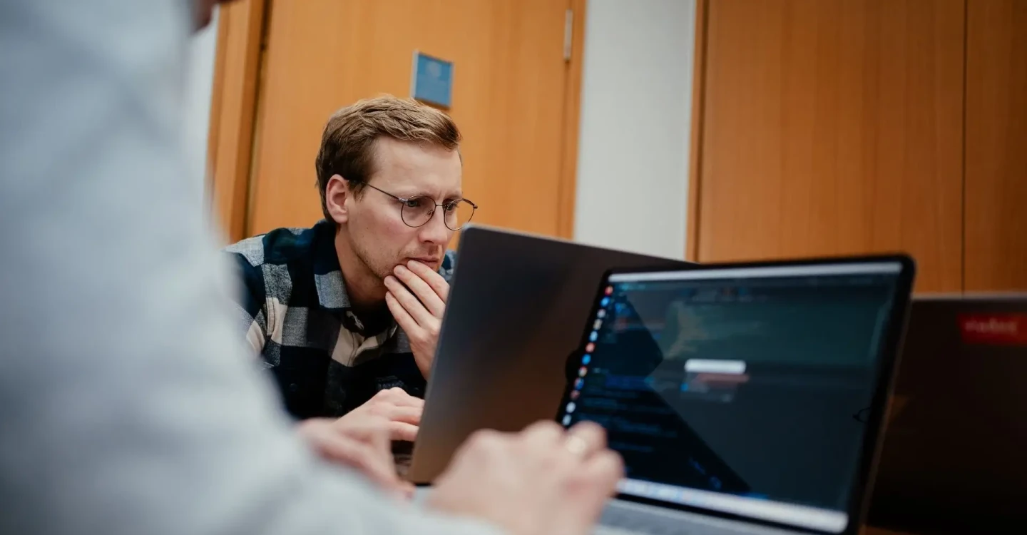 Zwei Mitarbeiter der viadee sitzen mit ihren Laptops an einem Tisch und arbeiten.