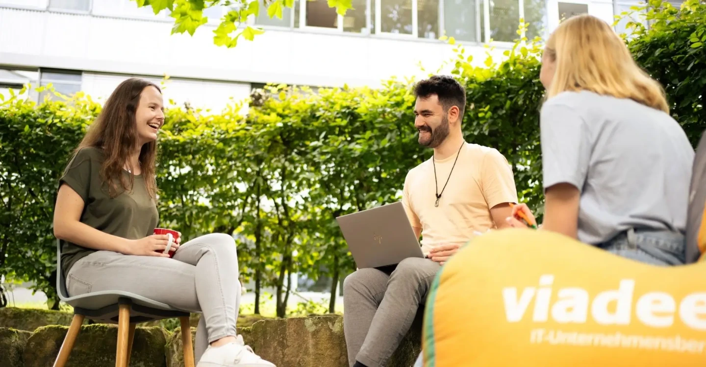 Drei Werkstudierende der viadee sitzen im Garten. Sie arbeiten zusammen.