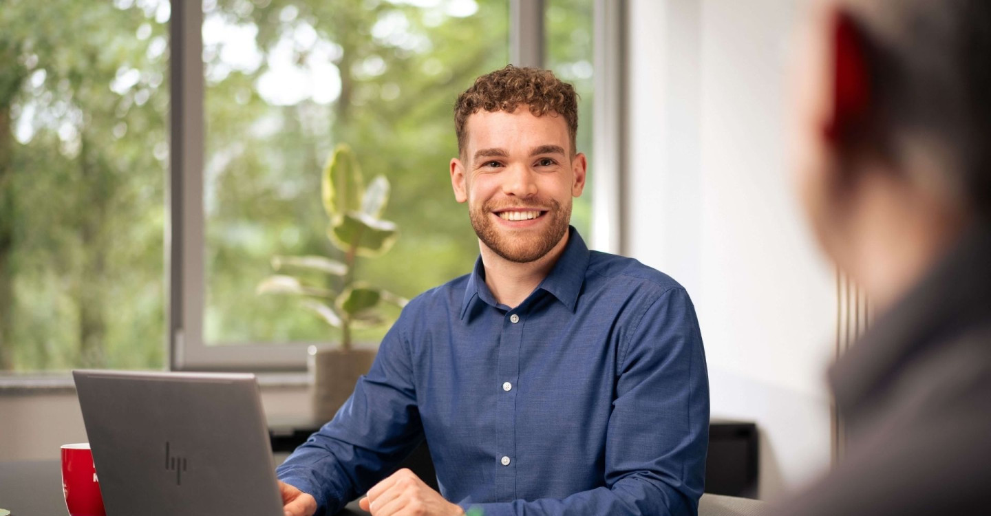 Ein Werkstudent der viadee sitzt mit einem Kollegen an einem Schreibtisch und lächelt.