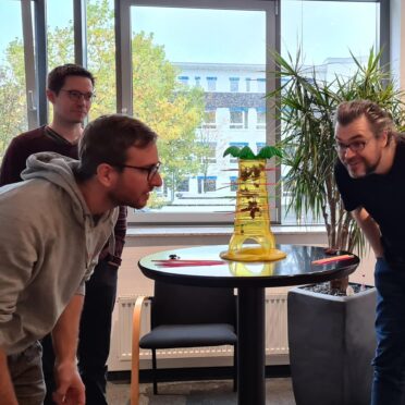 Drei Seminar-Teilnehmende stehen in einem Seminarraum und spielen ein Spiel.